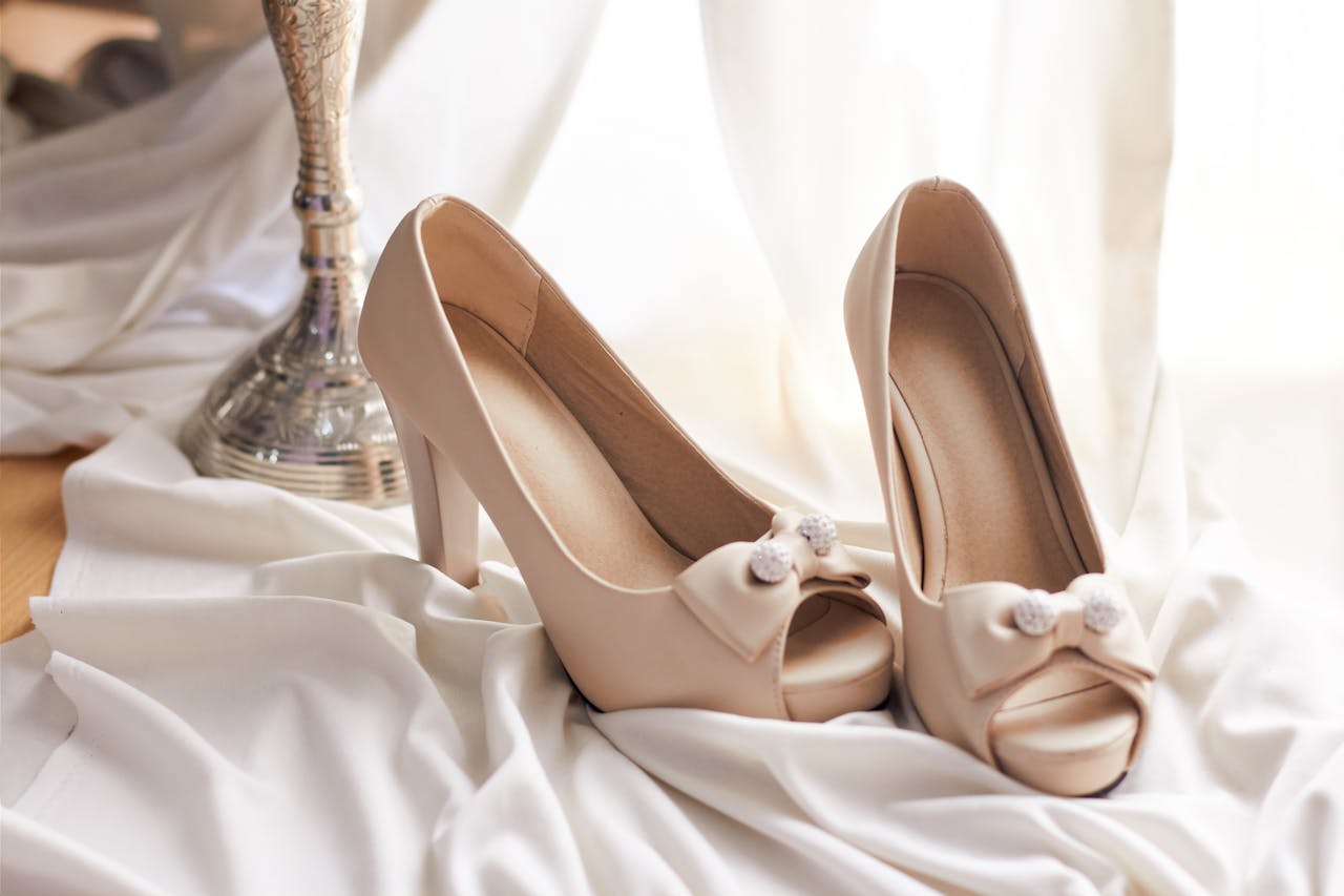 Close-up of elegant beige high heels with pearl decorations placed on white satin fabric indoors.